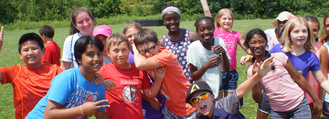A group of children smiling and posing together on the grass in Central Massachusetts