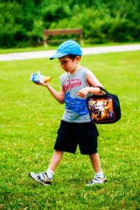 A young boy at the summer camp in Central Massachusetts, holding a lunch bag and a toy.