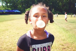 A young girl blowing a chewing and posing for a picture during YMCA camp in Central Massachusetts