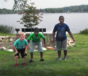 Three boys pose smiling in front of a lake during summer camp in Central Massachusetts.