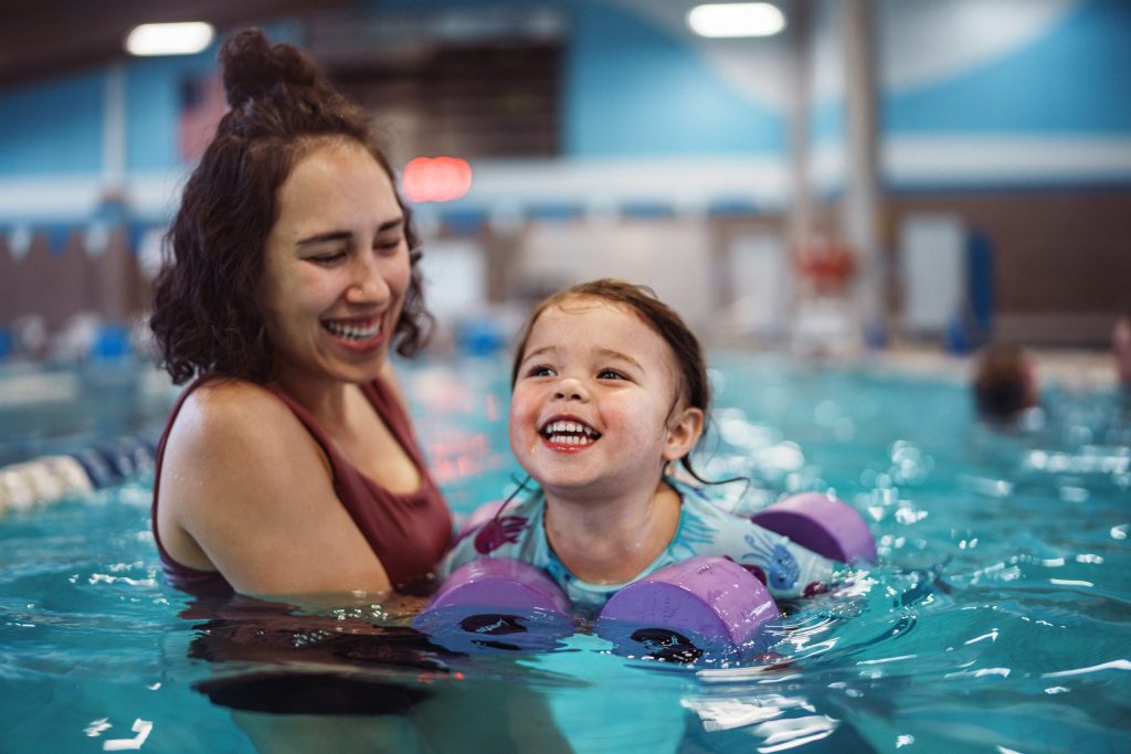 Smiling girl learns how to swim with the help of her Mother