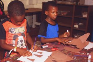 Two young boys create paper crafts at a table during a summer camp in Central Massachusetts.