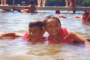 Two young boys wearing life jackets play in the water at a summer camp in Central Massachusetts.