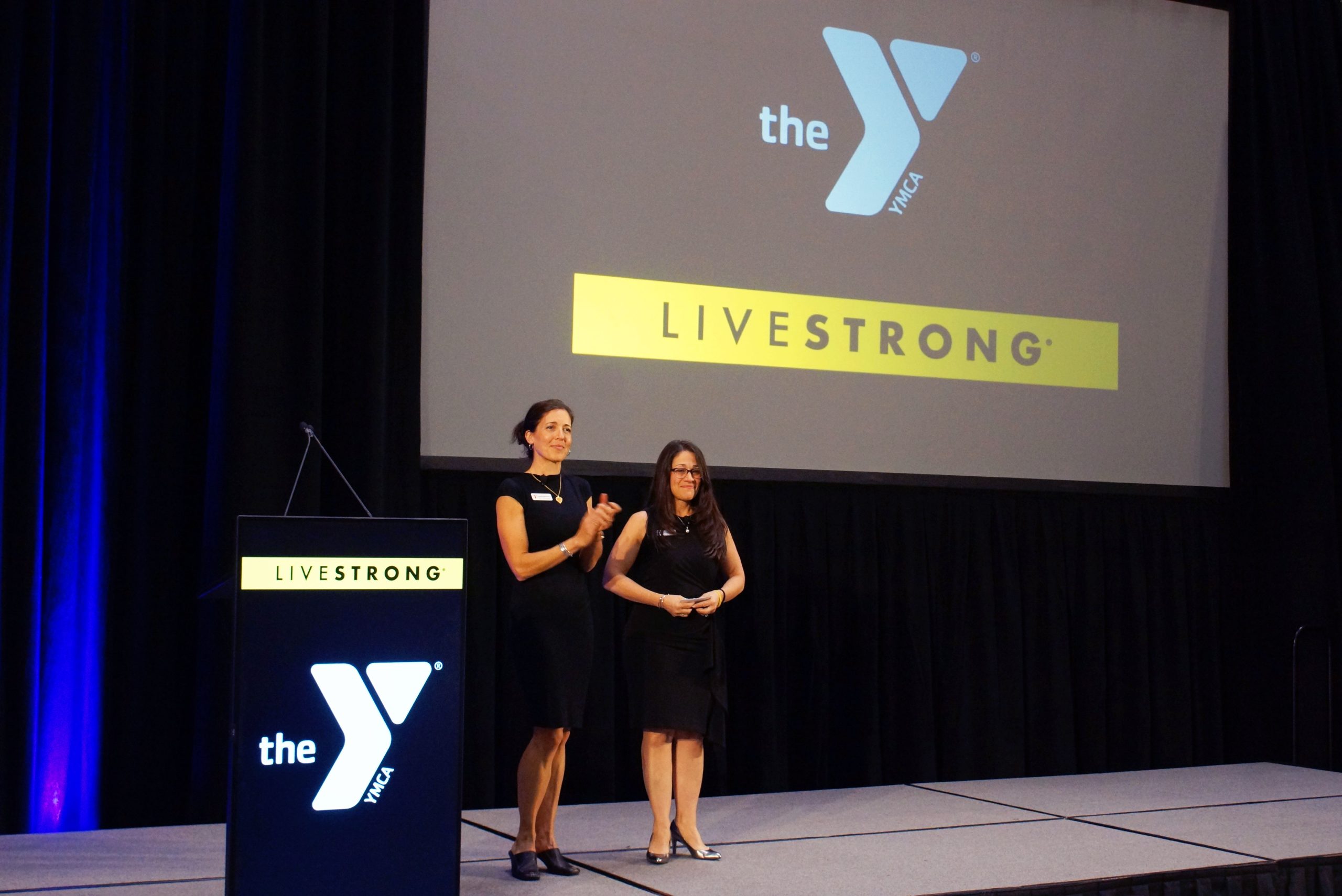 DSC02750-edit-1 Two women are present at a podium with the YMCA Event on stage in Central Massachusetts.