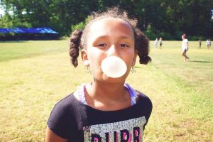 A young girl in grass blowing a bubble at YMCA Camp Lowe in Central Massachusetts
