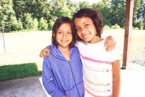 Two young girls stand together in front of a house at YMCA Camp Lowe, Central Massachusetts