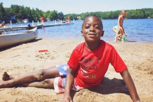 Young boy sitting in sand at YMCA Camp Lowe beach in Central Massachusetts