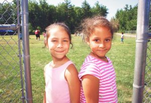 Two kids standing near a chain-link fence on a grassy field at YMCA Camp Lowe in Central Massachusetts