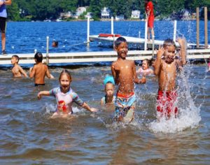Kids splashing and playing in shallow lake water near a dock at YMCA Camp Lowe in Central Massachusetts