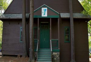 Brown wooden building with green doors and YMCA logo at Camp Lowe in Central Massachusetts