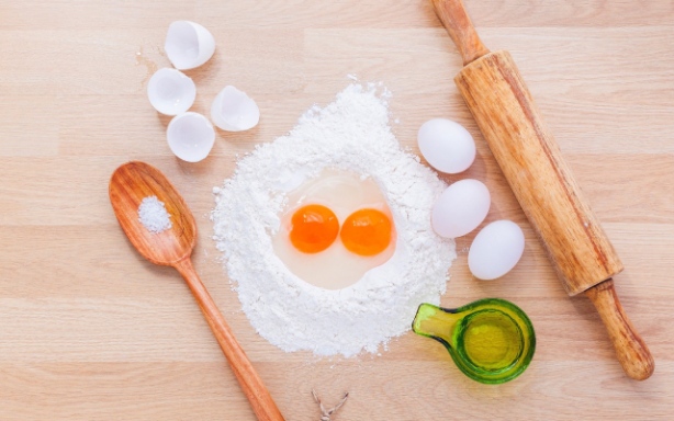 Baking ingredients, including flour, eggs, and a rolling pin, on a wooden table