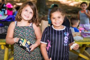 Two individuals are enjoying snacks outdoors, at a summer camp in Central Massachusetts
