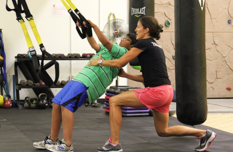 A youth and a personal trainer using suspension exercise straps in a gym