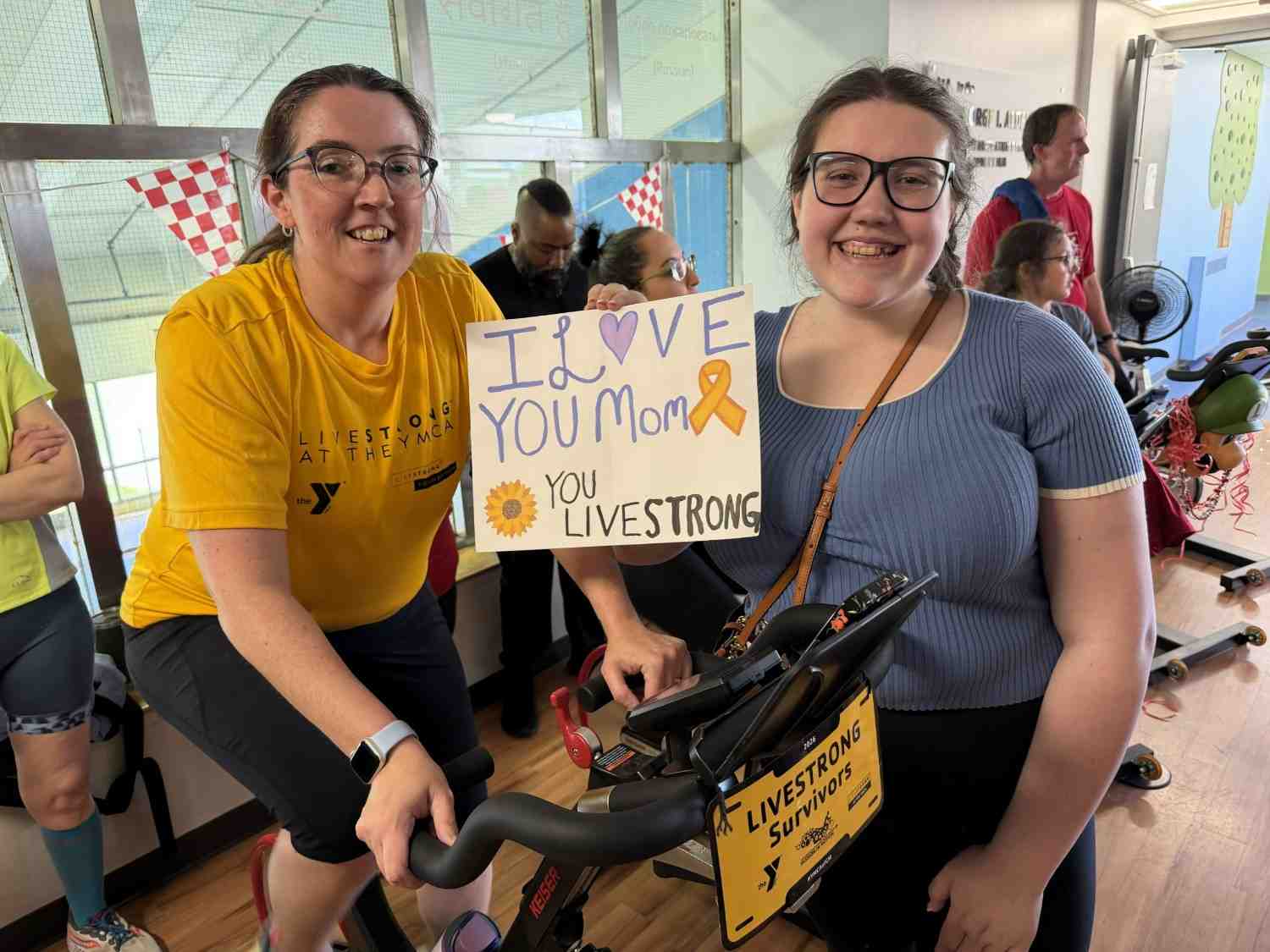 YMCA participants holding Livestrong support sign during indoor cycling Mission in Motion event