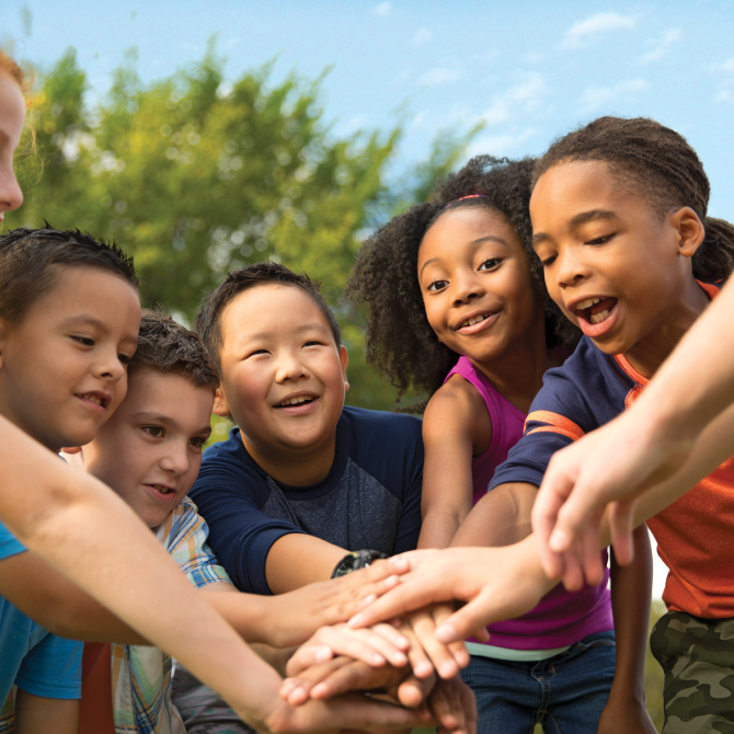 A group of children at summer camp in Central Massachusetts, smiling and joining hands.